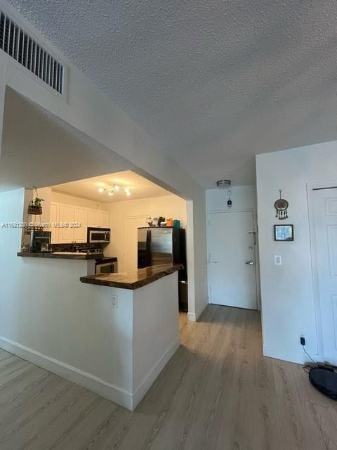 kitchen with white cabinetry, stainless steel appliances, hardwood / wood-style floors, a textured ceiling, and kitchen peninsula