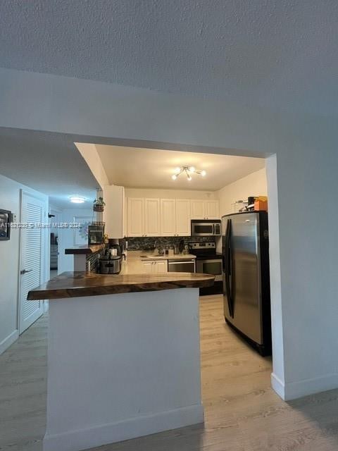 kitchen featuring white cabinetry, tasteful backsplash, stainless steel appliances, light hardwood / wood-style flooring, and kitchen peninsula