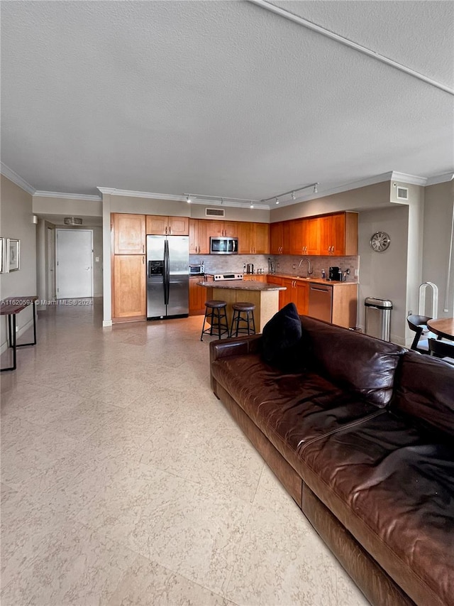 living room featuring light tile patterned flooring, a textured ceiling, track lighting, sink, and ornamental molding