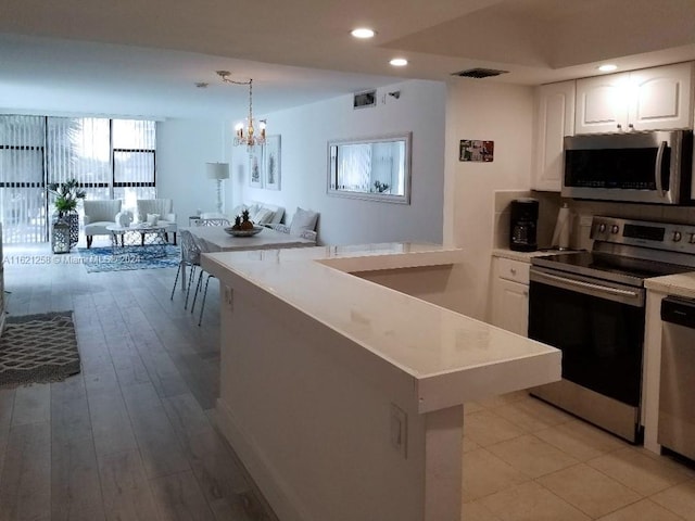 kitchen featuring stainless steel appliances, white cabinets, pendant lighting, light hardwood / wood-style floors, and a chandelier