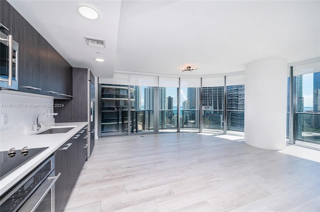 kitchen featuring sink, stainless steel oven, floor to ceiling windows, black electric cooktop, and light hardwood / wood-style flooring