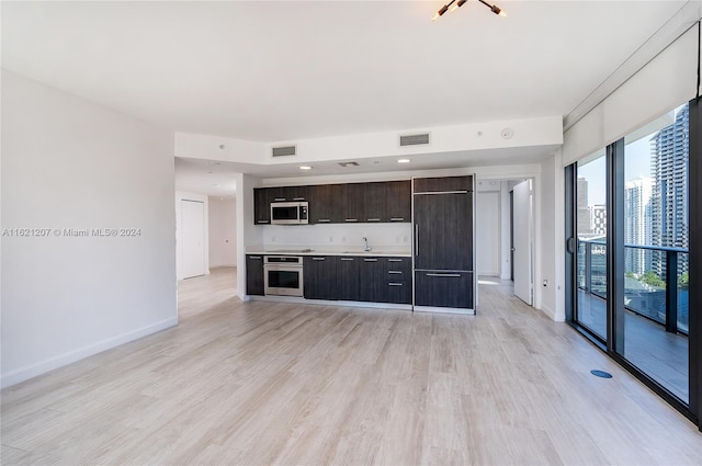 kitchen with stainless steel appliances, sink, dark brown cabinets, and light hardwood / wood-style flooring