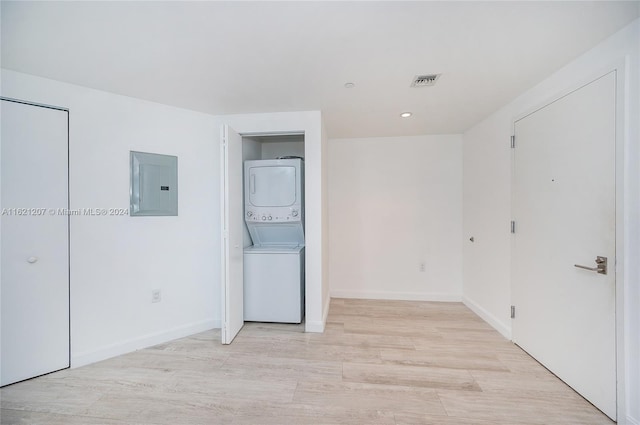 spare room featuring stacked washer and dryer, electric panel, and light hardwood / wood-style floors