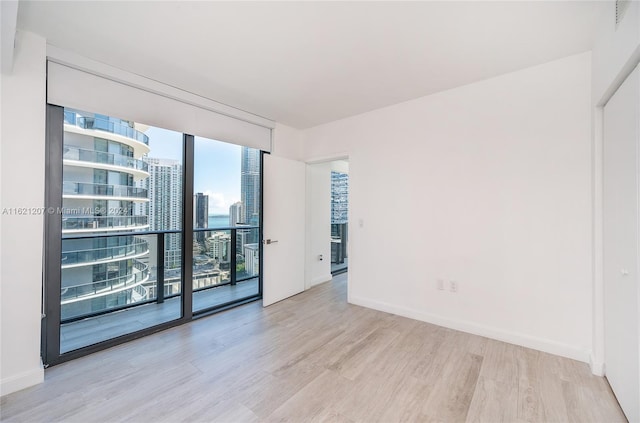 empty room with floor to ceiling windows and light hardwood / wood-style floors