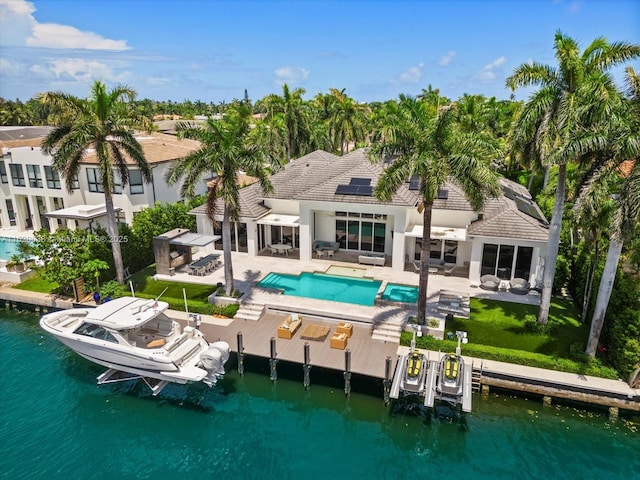 back of house featuring roof mounted solar panels, boat lift, a patio area, and an outdoor pool