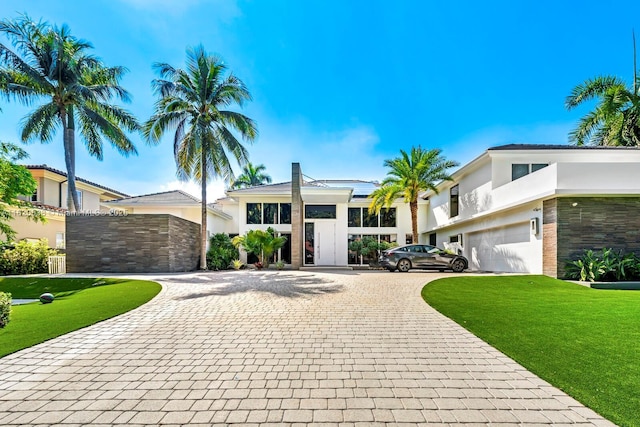 view of front of home featuring curved driveway, stucco siding, an attached garage, and a front yard