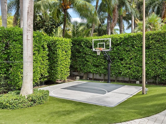 view of basketball court featuring a lawn, basketball hoop, and fence