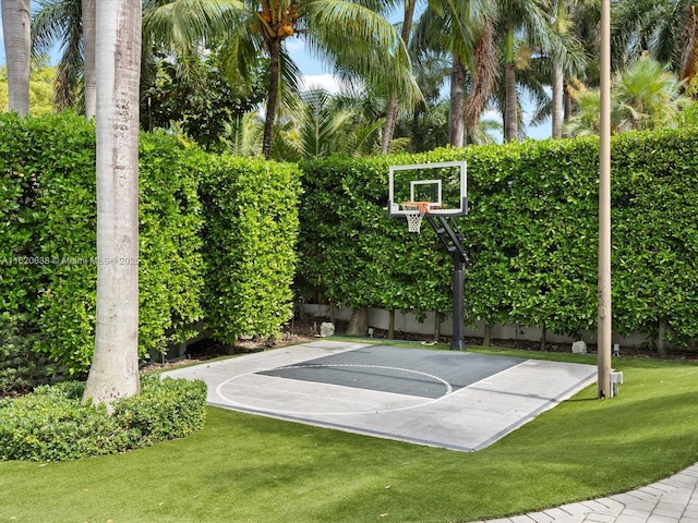view of sport court featuring basketball hoop and a lawn