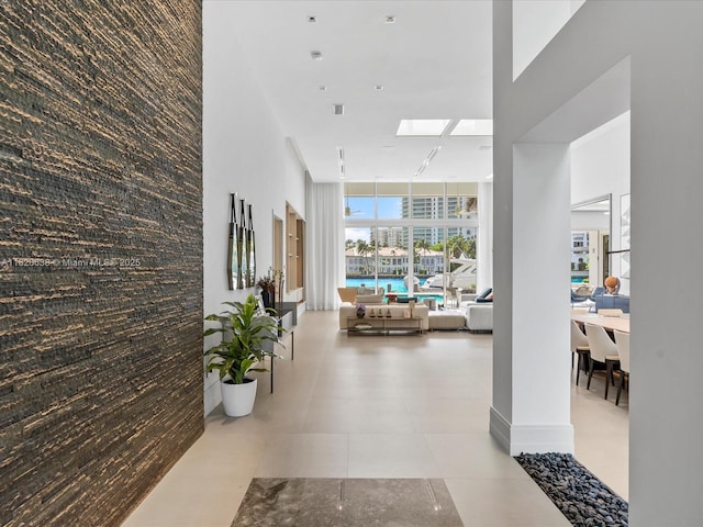 hall featuring light tile patterned floors, an accent wall, visible vents, a towering ceiling, and floor to ceiling windows