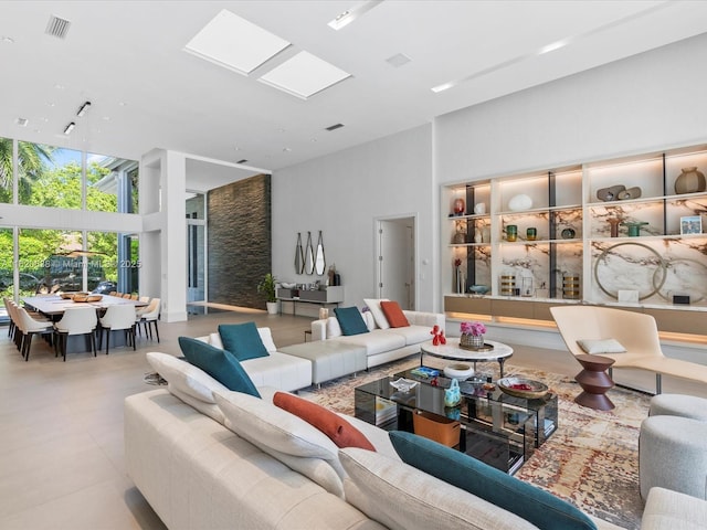 living room with a skylight, visible vents, a towering ceiling, and light tile patterned floors