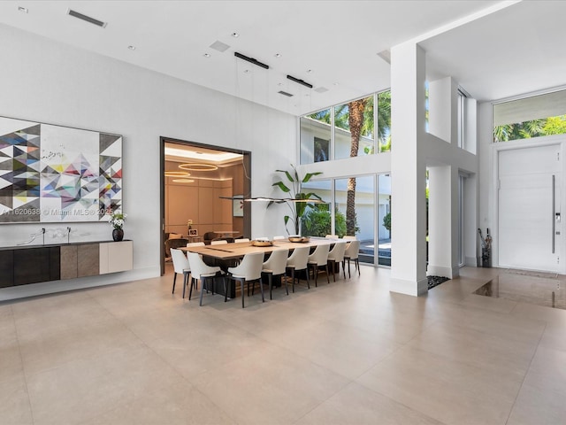 dining room with a towering ceiling, baseboards, visible vents, and a wall of windows