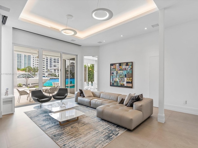 living area with a tray ceiling, visible vents, a city view, and baseboards