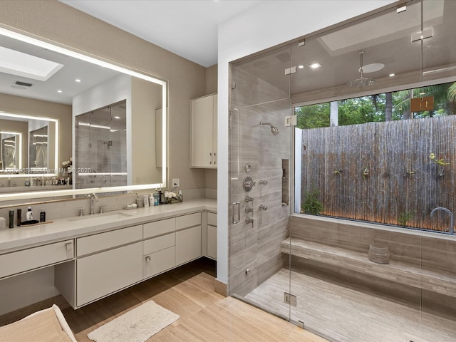 full bath featuring a skylight, visible vents, vanity, a shower stall, and wood finished floors