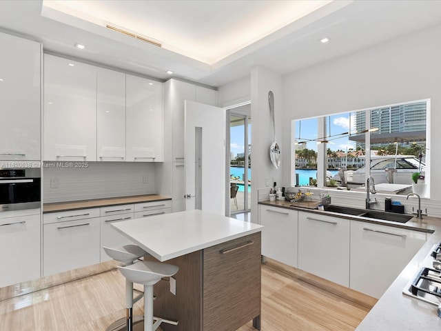 kitchen with white cabinets, a breakfast bar, a water view, light countertops, and stainless steel oven