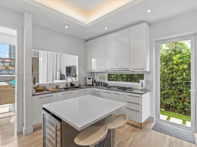 kitchen featuring wine cooler, dark countertops, stainless steel gas stovetop, white cabinets, and a sink