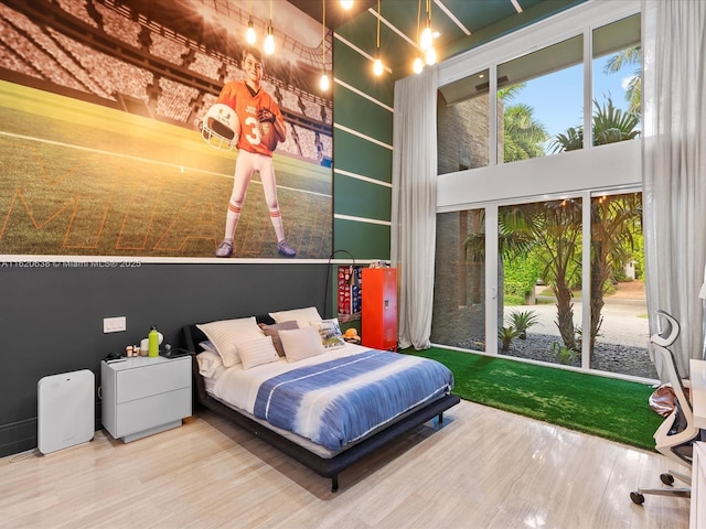 bedroom with access to outside, wood finished floors, and a towering ceiling