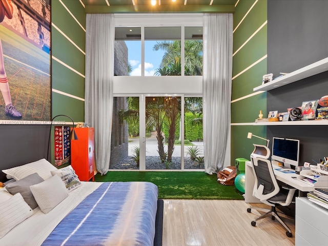 bedroom with multiple windows, a high ceiling, and wood finished floors