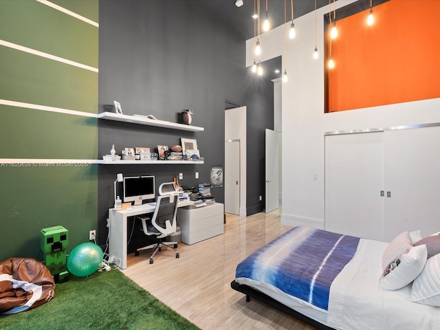 bedroom featuring a closet, light wood-type flooring, and a towering ceiling