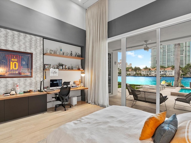bedroom with a high ceiling, built in study area, access to exterior, wood finished floors, and expansive windows