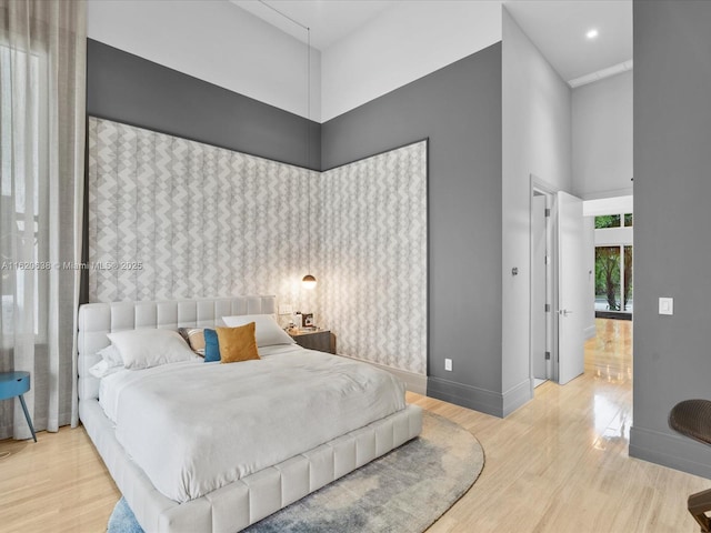 bedroom with light wood-style floors, a high ceiling, and baseboards