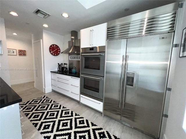 kitchen featuring white cabinetry, light hardwood / wood-style flooring, wall chimney exhaust hood, and stainless steel appliances