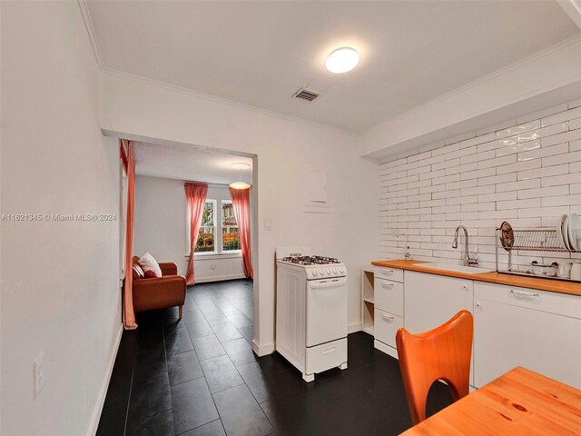 kitchen with dark tile patterned floors, tasteful backsplash, white cabinets, white range with gas cooktop, and sink