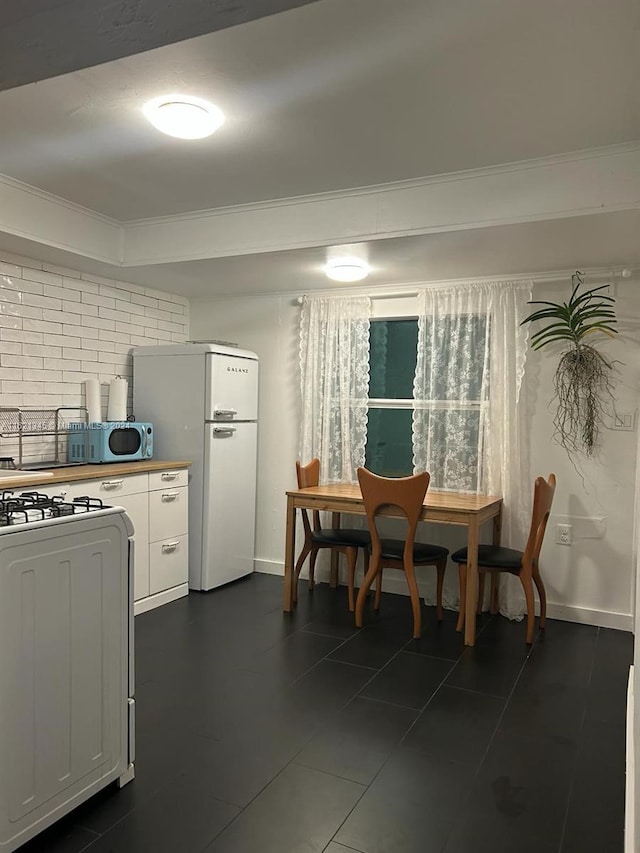 kitchen with crown molding, range with gas stovetop, white refrigerator, and white cabinetry