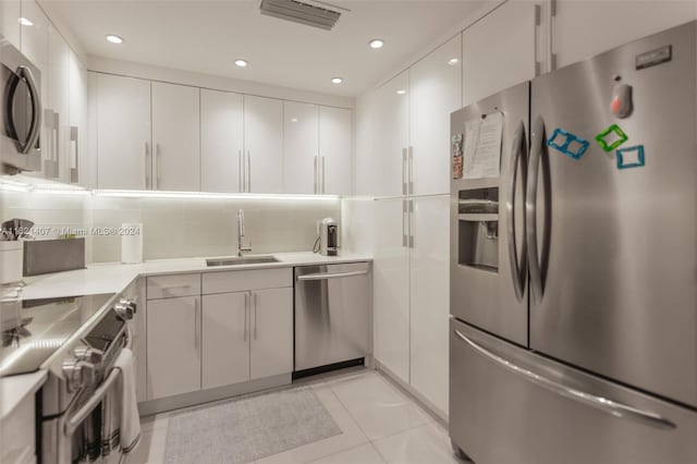 kitchen with sink, white cabinets, decorative backsplash, light tile patterned floors, and stainless steel appliances