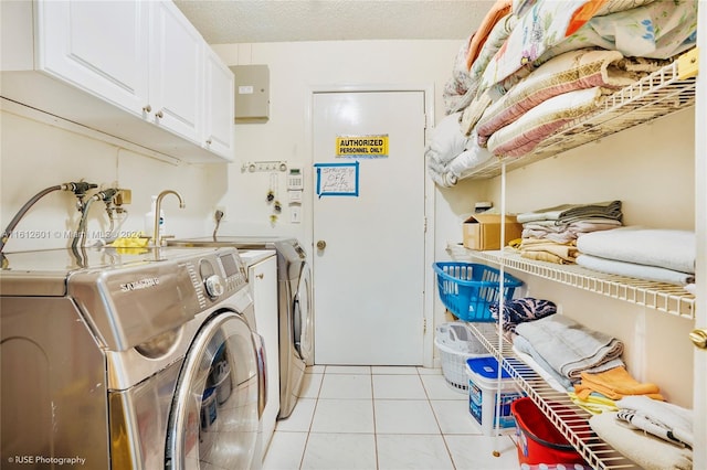 laundry room with a textured ceiling, separate washer and dryer, cabinets, and light tile patterned floors