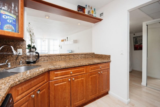 kitchen featuring light stone counters, decorative backsplash, a sink, and brown cabinets