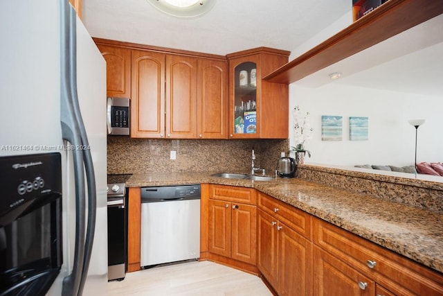 kitchen with decorative backsplash, appliances with stainless steel finishes, stone countertops, glass insert cabinets, and a sink