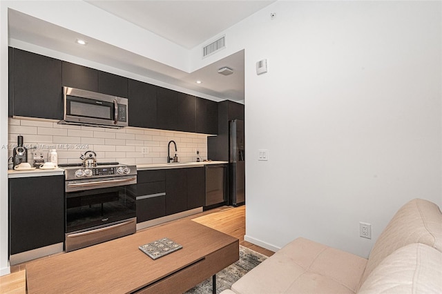 kitchen with sink, appliances with stainless steel finishes, decorative backsplash, and light wood-type flooring