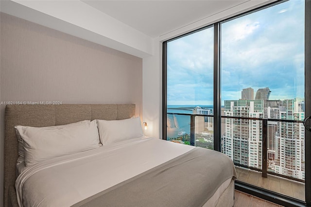 bedroom with a water view, hardwood / wood-style flooring, multiple windows, and a wall of windows