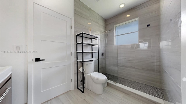 bathroom with toilet, a tile shower, and vanity