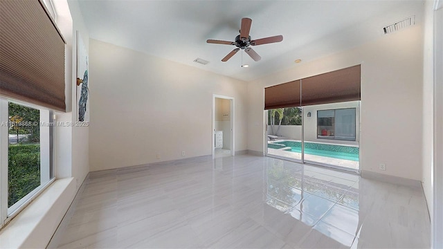 empty room with a wealth of natural light, ceiling fan, and light tile patterned floors