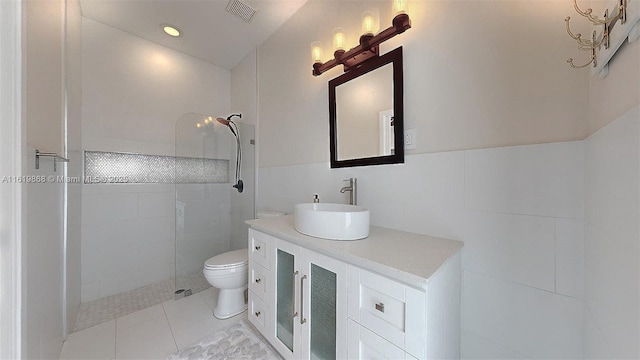 bathroom featuring vanity, tile patterned flooring, toilet, tiled shower, and tile walls