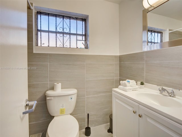 bathroom with vanity, toilet, a wealth of natural light, and tile walls