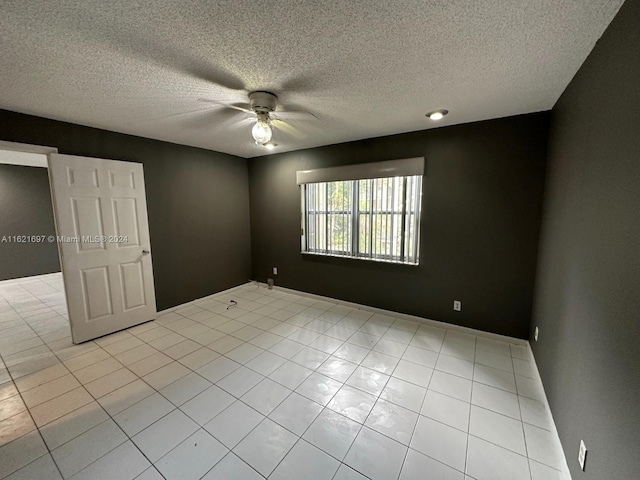 tiled empty room featuring ceiling fan and a textured ceiling