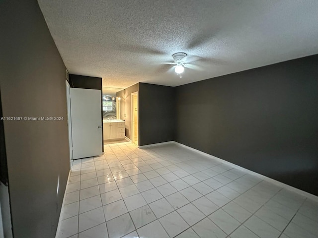 empty room featuring a textured ceiling, light tile patterned floors, and ceiling fan