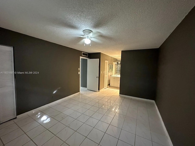 unfurnished bedroom featuring a closet, connected bathroom, ceiling fan, a textured ceiling, and light tile patterned floors