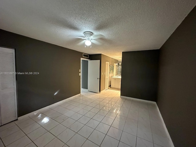 unfurnished bedroom featuring a closet, ceiling fan, ensuite bath, a textured ceiling, and light tile patterned floors