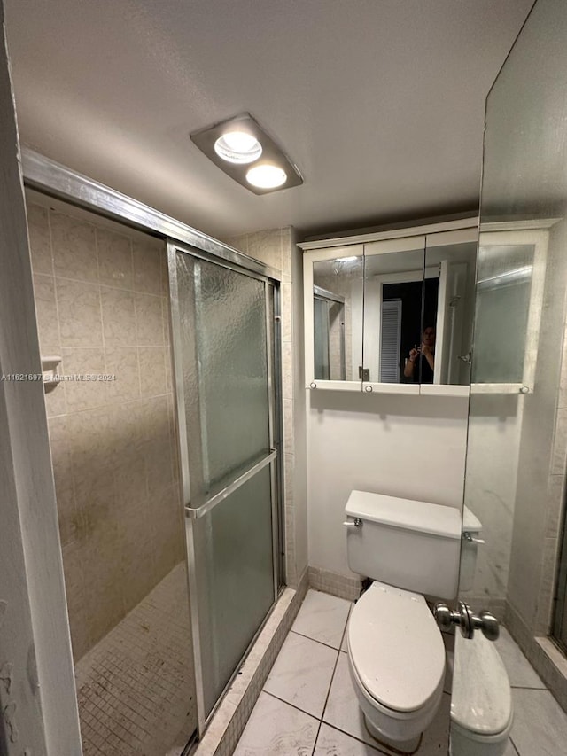 bathroom featuring a shower with door, tile patterned flooring, and toilet