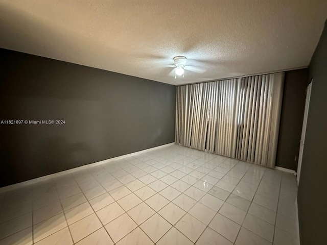 empty room with light tile patterned flooring, ceiling fan, and a textured ceiling