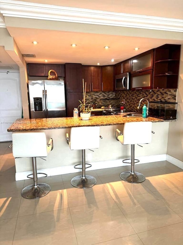 kitchen with dark tile patterned floors, a breakfast bar area, backsplash, and stainless steel appliances