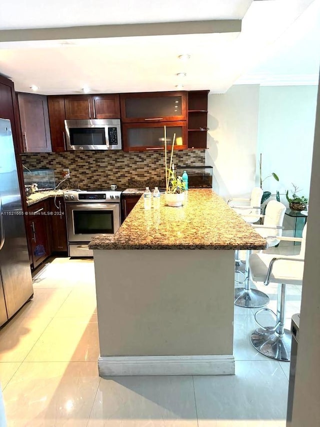 kitchen with tasteful backsplash, stainless steel appliances, a center island with sink, light stone counters, and light tile patterned floors