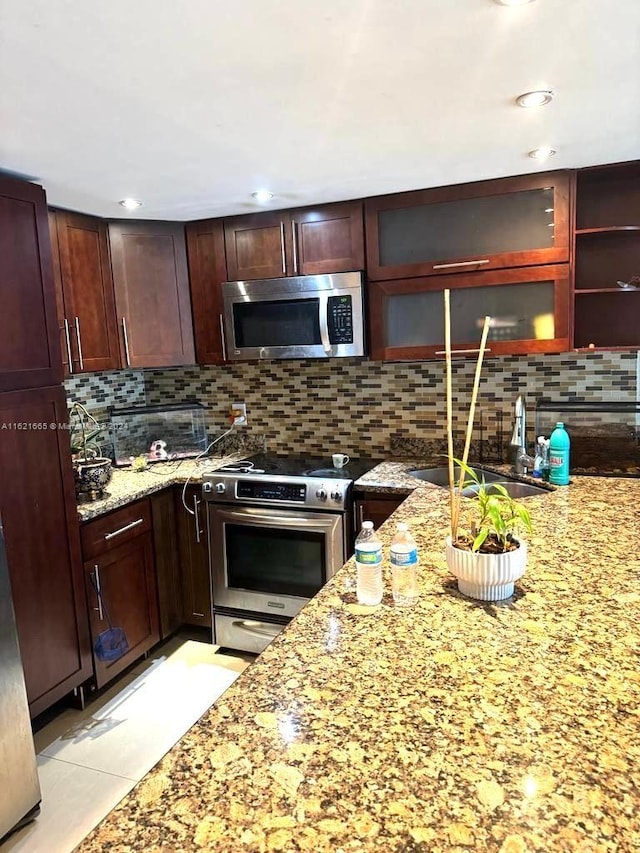 kitchen with light tile patterned flooring, tasteful backsplash, light stone counters, appliances with stainless steel finishes, and sink