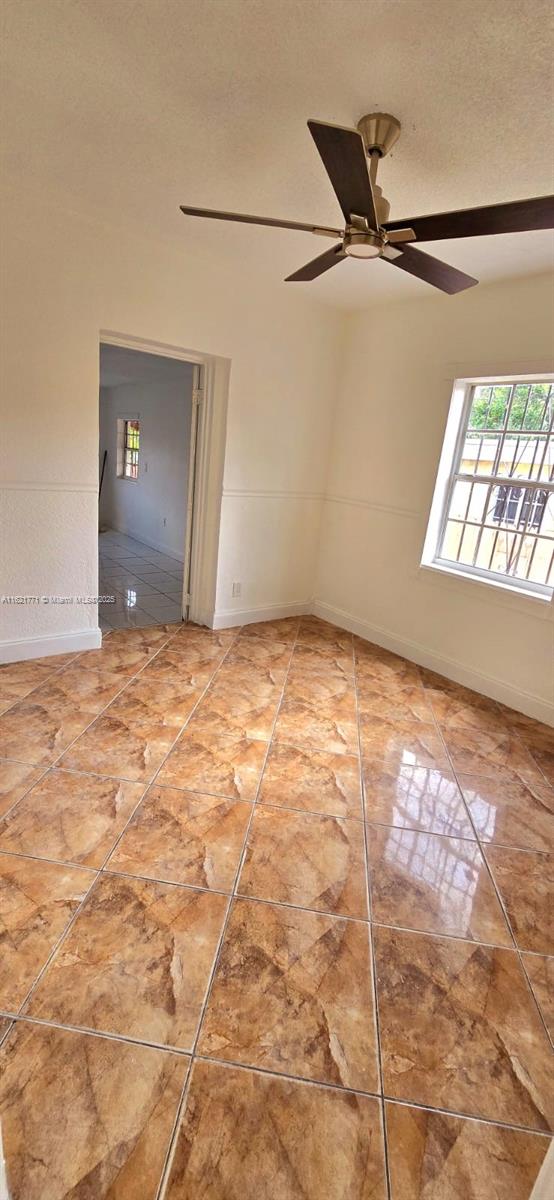 empty room with tile patterned floors, ceiling fan, and a textured ceiling