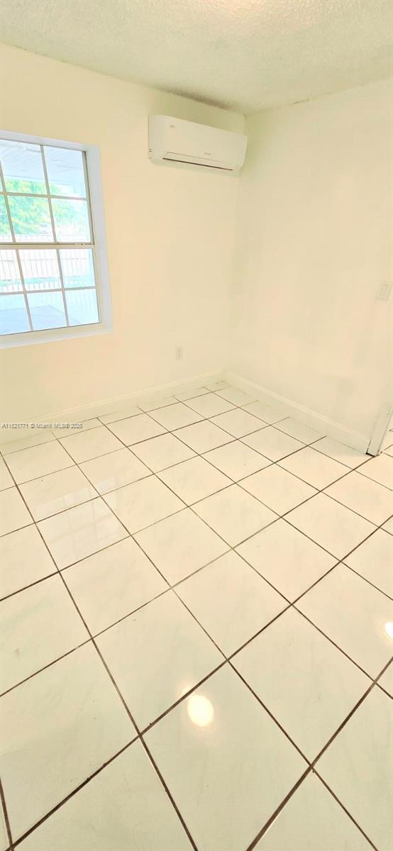 unfurnished room with light tile patterned flooring, an AC wall unit, and a textured ceiling