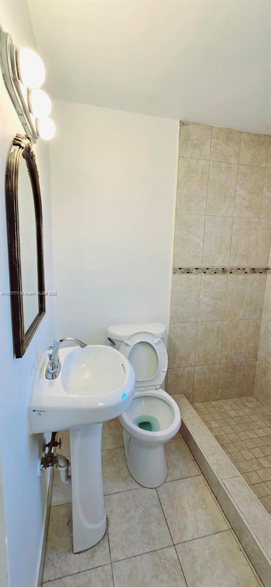 bathroom with tile patterned flooring, toilet, and a tile shower