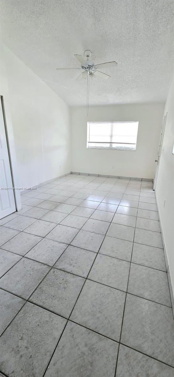 spare room featuring ceiling fan, light tile patterned flooring, and a textured ceiling